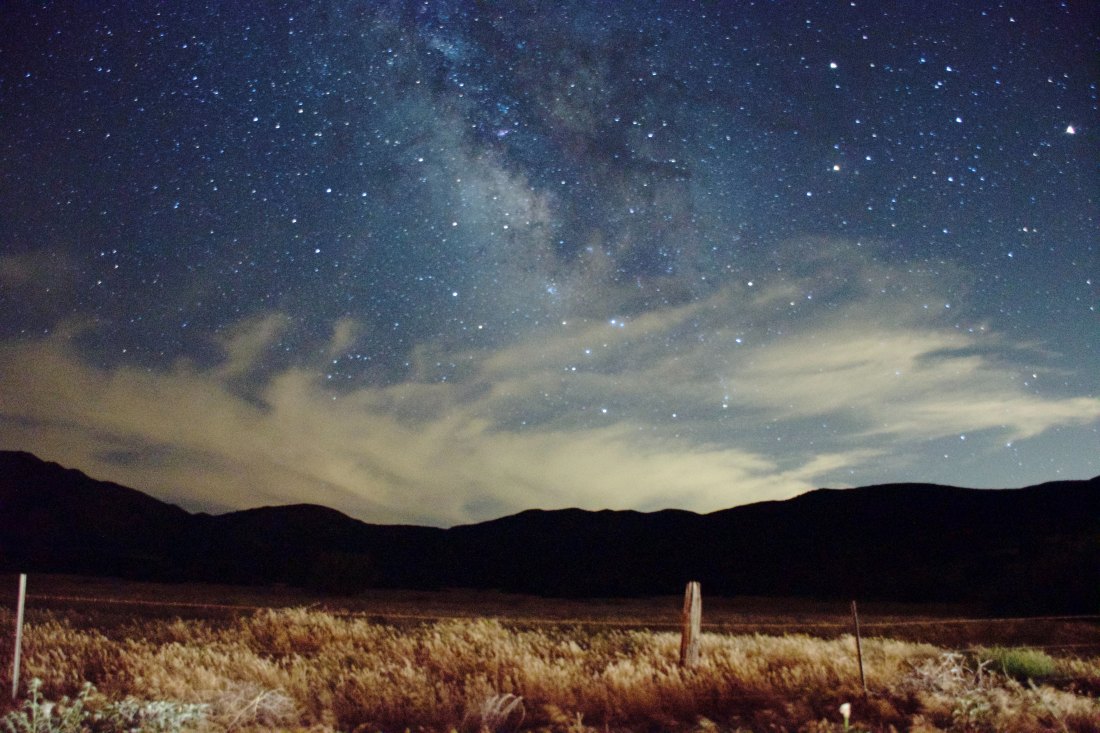 Cloudy sky with some stars over mountains.